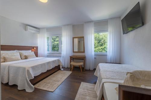a bedroom with two beds and a tv and two windows at Up27 Suites Plitvice in Plitvička Jezera