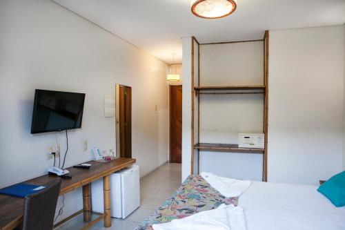 a room with a bed and a desk and a television at Pousada Sol e Mar in Juquei