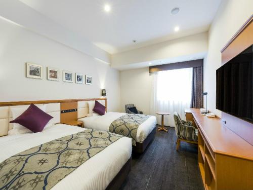 a hotel room with two beds and a desk at HOTEL MYSTAYS Sapporo Aspen in Sapporo