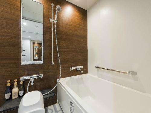 a bathroom with a tub and a toilet and a mirror at HOTEL MYSTAYS Sapporo Aspen in Sapporo