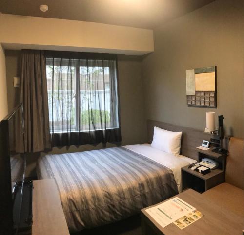 a hotel room with a bed and a window at Hotel Route-Inn Nakano in Nakano