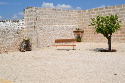 a wooden bench next to a brick wall with a tree at Masseria Il Vignale in Ostuni