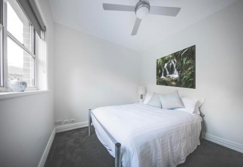 a white bedroom with a bed and a ceiling fan at Diggers Beach Cottage in Coffs Harbour