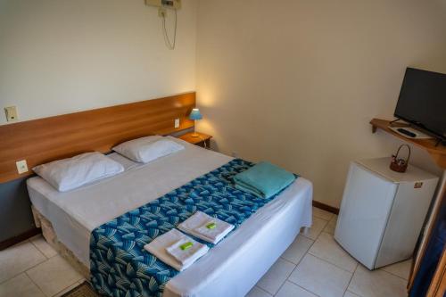 a bedroom with a bed with two towels and a television at Pousada Piquara in Mangaratiba