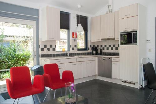 a kitchen with white cabinets and red chairs at Bungalowpark Het Verscholen Dorp in Harderwijk