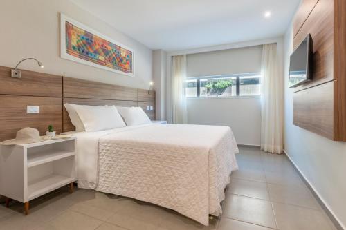 a bedroom with a white bed and a television at Intercity Maceio in Maceió