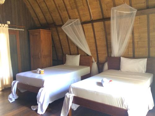 2 camas en una habitación con sábanas blancas en Melati Cottage, en Gili Trawangan