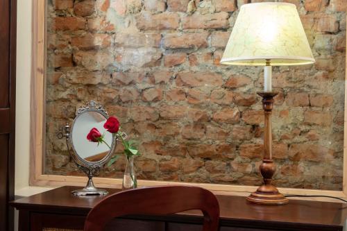 a table with a lamp and a mirror and a flower in a vase at De Hoek Manor in Stellenbosch