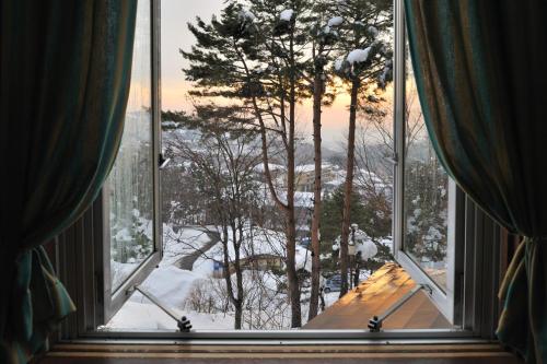 a window with a view of a snow covered forest at Mogamitakayu Zenshichinoyu Ohira in Zao Onsen
