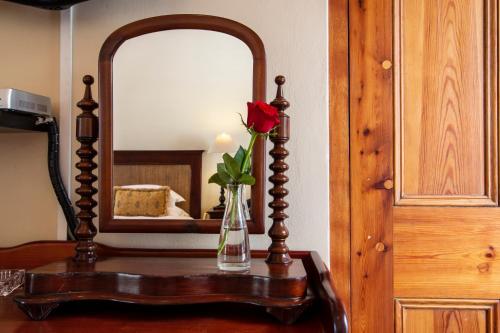 a vase with a rose on a table in front of a mirror at De Hoek Manor in Stellenbosch