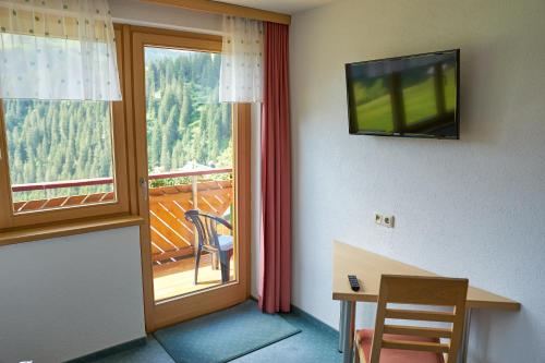 Zimmer mit einem Balkon, einem TV und einem Schreibtisch. in der Unterkunft dr'Berghof in Damüls