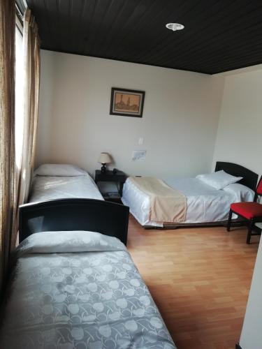 a bedroom with two beds and a red chair at Hotel Oicatá in Duitama