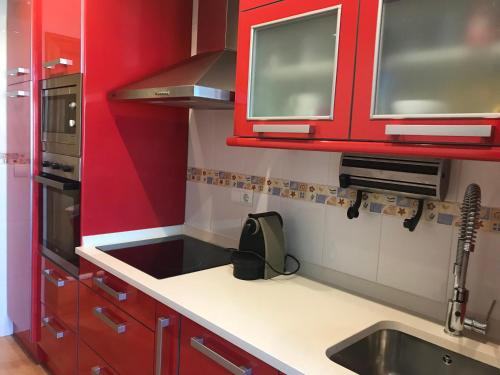 una cocina con armarios rojos y fregadero en apartamento con jardín privado y barbacoa a 5 min playas santander, en Santander
