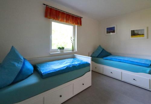 2 Betten in einem Zimmer mit blauen Kissen und einem Fenster in der Unterkunft Ferienhaus Annemiete in Putbus