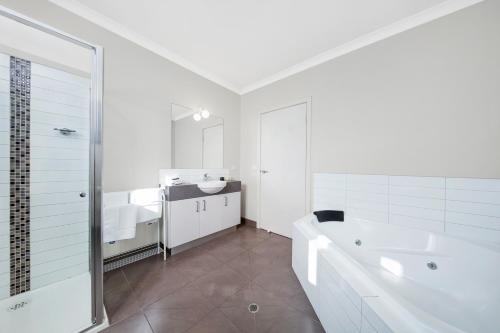 ein weißes Badezimmer mit einer Badewanne und einem Waschbecken in der Unterkunft Moonlight Bay Apartments in Rye
