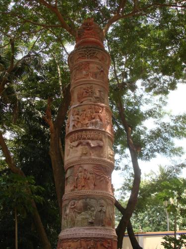 a tall pillar with paintings on it next to a tree at Indeco Hotels Swamimalai in Kumbakonam