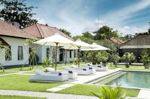 een groep witte stoelen en parasols naast een zwembad bij Teges Asri by Bukit Vista in Uluwatu