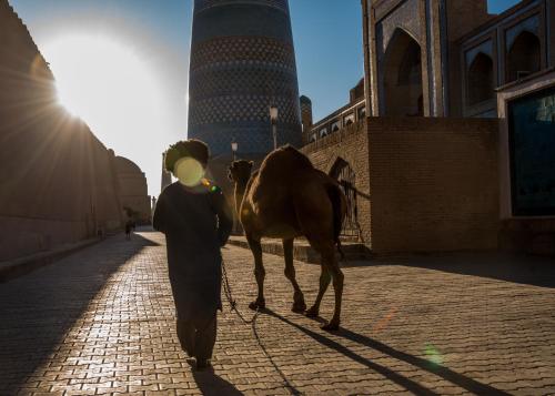 a man walking a camel down a street at Orient Star Khiva Hotel- Madrasah Muhammad Aminkhan 1855 in Khiva