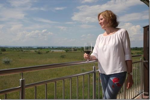 a woman standing on a balcony holding a glass of wine at Gästehaus Lackenblick in Illmitz