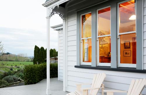 a white house with two white chairs on a porch at Maungakawa Villa in Cambridge
