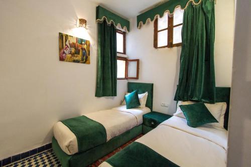 two beds in a room with green curtains at Riad Dar Bab Guissa in Fès