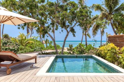 an outdoor swimming pool with an umbrella and a beach at Six Senses Fiji in Malolo