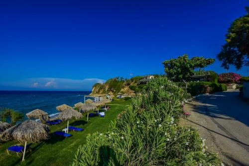 a row of straw umbrellas on a lawn next to the ocean at Porto Giardino Apartments in Kipseli