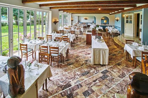 ein Restaurant mit weißen Tischen, Stühlen und Fenstern in der Unterkunft Hotel Villa Rainer in Pörtschach am Wörthersee