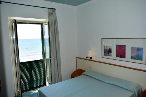 a bedroom with a bed and a window with the ocean at Hotel Amyclae in Sperlonga