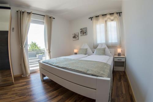 a white bedroom with a large bed and a window at Apartments Mojeljeto in Fažana
