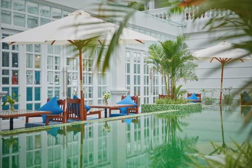 a pool with tables and umbrellas next to a building at Manoir Des Arts Hotel in Hai Phong