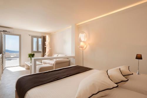 a white bedroom with a bed and a chair at Galaxy Suites & Villas in Imerovigli