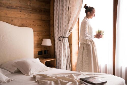 a woman in a dress standing next to a bed at Auberge De La Maison in Courmayeur