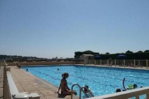 une femme assise à côté d'une grande piscine dans l'établissement Residence des Coteaux du Preconil, à Sainte-Maxime