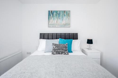 a white bedroom with a large bed with blue pillows at Elthorne Luxury Apartments - Uxbridge in Uxbridge