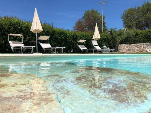 a swimming pool with chairs and umbrellas at Masseria Paglieroni in Martina Franca