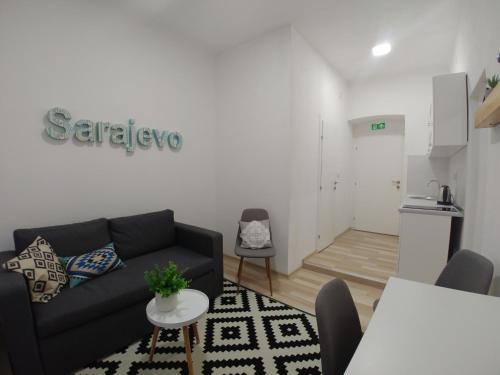 a living room with a black couch and a kitchen at Apartments Sari in Sarajevo