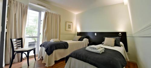 Habitación con 2 camas, silla y ventana en Abril Hotel Boutique en Mendoza