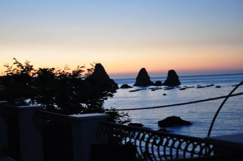 a sunset over the ocean with rocks in the water at La Terrazza in Aci Castello