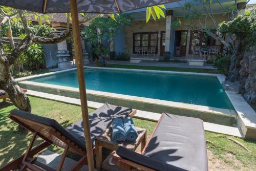 a chair and an umbrella next to a swimming pool at Koming Guest House in Canggu