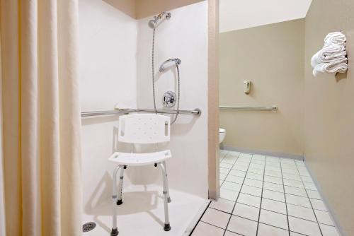 Microtel Inn & Suites by Wyndham Joplin في جوبلين: كرسي أبيض في حمام مع دش