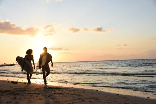 a man and woman walking on the beach with a surfboard at Veranda Tamarin Hotel & Spa in Tamarin