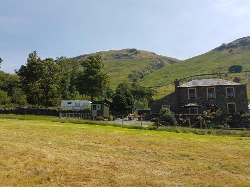 a house with a field in front of a hill at Shepherds hut Dolly wagon in Keswick