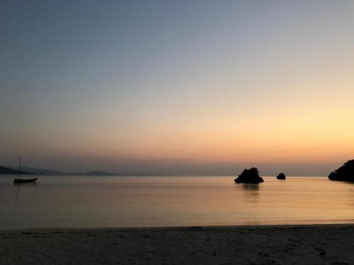 a sunset on the beach with rocks in the water at Pine Shima Resort Coral Fish in Ibaruma