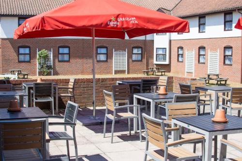 a patio with tables and chairs and a red umbrella at Dragonfly Hotel Bury St Edmunds in Bury Saint Edmunds