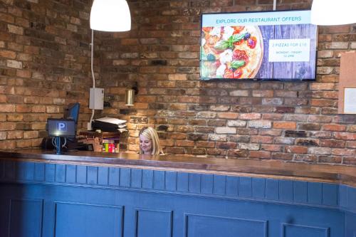 a woman sitting at the counter of a pizza restaurant at Dragonfly Hotel Bury St Edmunds in Bury Saint Edmunds