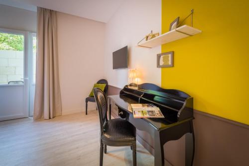 a living room with a piano and a yellow wall at The Originals Boutique, Hôtel Le Londres, Saumur in Saumur