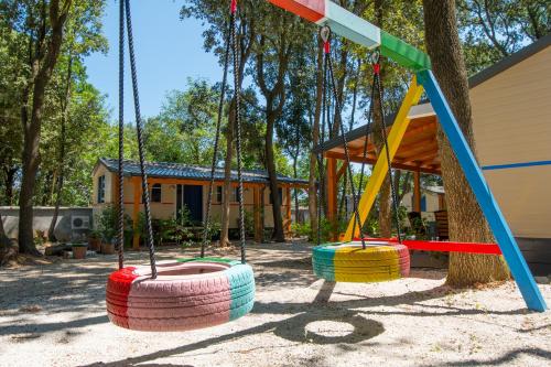três baloiços num parque infantil com uma casa ao fundo em Mobile home - Kamp Olga em Banjole