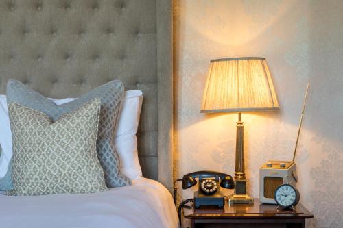 a bed with a lamp and a clock on a table at Eastwell Manor, Champneys Hotel & Spa in Ashford