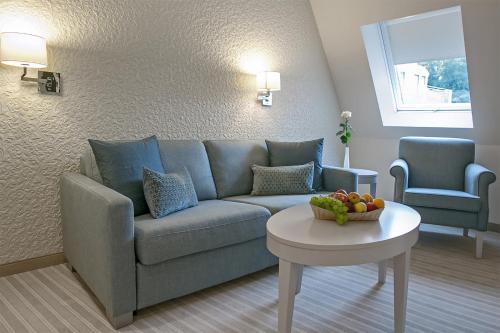 a living room with a couch and a bowl of fruit on a table at Dorint Parkhotel Meißen in Meißen
